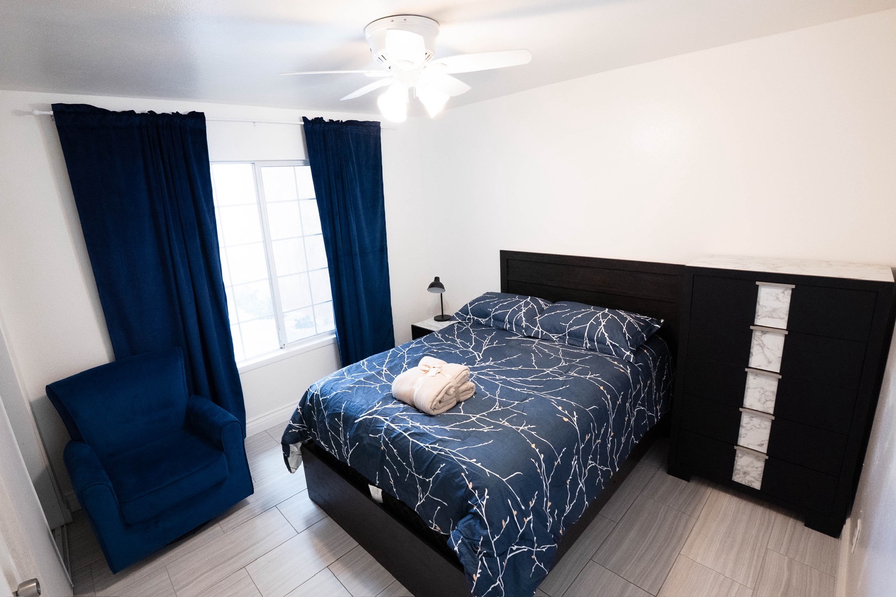 Cozy private bedroom with navy blue bedding, warm lighting, and a tidy, well-organized layout